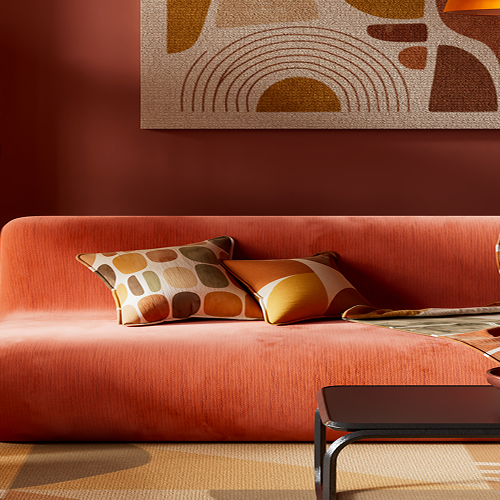 Wohnzimmer im Retro-Stil mit einem orangefarbenen Samtsofa, gemusterten Kissen und einer Decke, einer runden Stehlampe mit Rattanschirm, dunklem Holzregal und einem abstrakten Wandbild mit Bogenmuster über dem Sofa.
